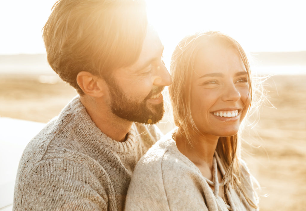 A man and a woman smile while at the beach at sunset