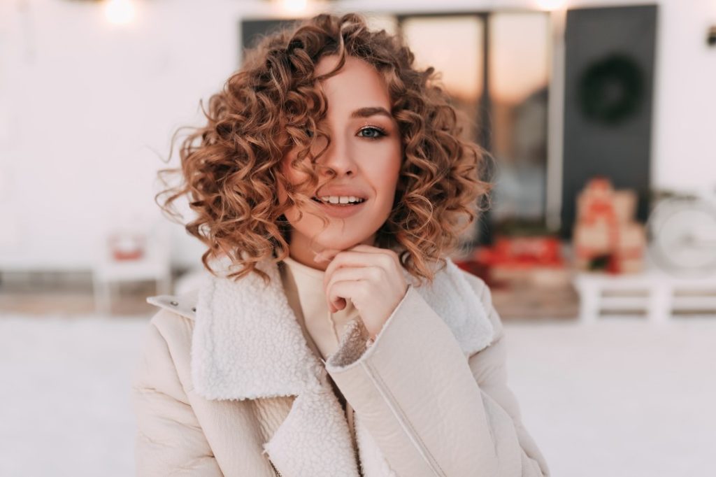 smiling woman with curly hair in a beige coat