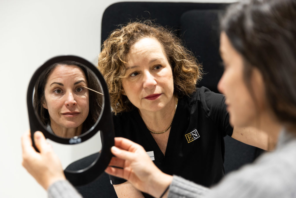 A woman looks at her face in a small circular mirror at Entre Nous Aesthetics in Menlo Park